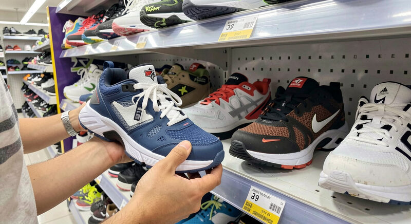 Dłonie trzymające but sportowy i porównujące jego podeszwę z drugim butem na sklepowej ladzie.